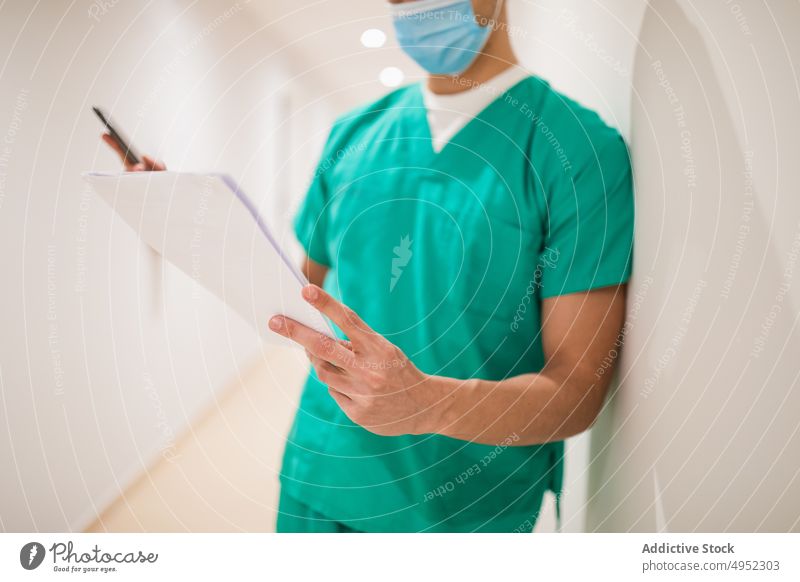 Arzt mit Papieren im Krankenhauskorridor lesen Uniform professionell Job steril achtsam Mann Gang Chirurg Licht Lampe glänzend Fokus Sanitäter Mundschutz