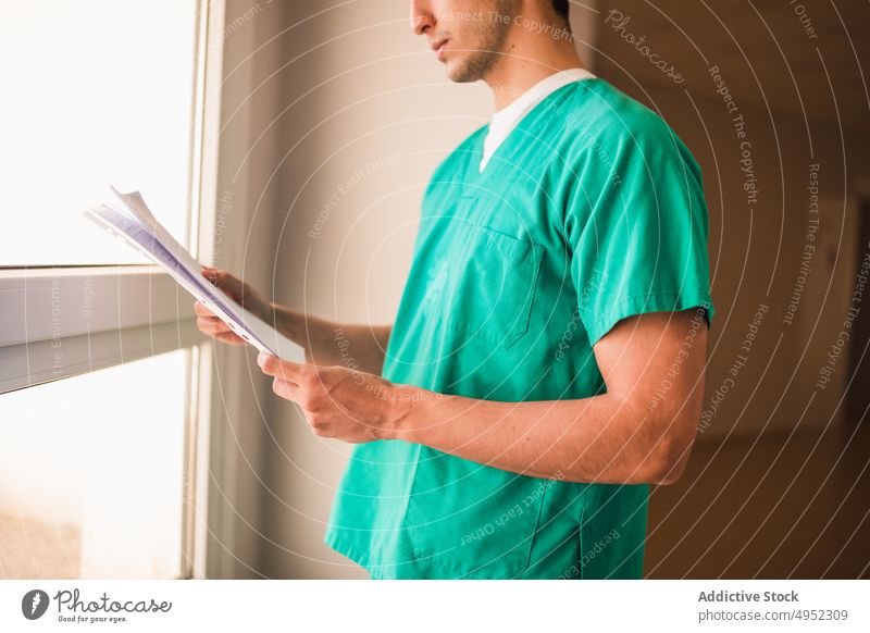 Uniformierter Arzt mit Papier auf dem Klinikflur Sanitäter Tür Beruf Chirurg behüten steril Mann Fenster Durchgang Krankenhaus professionell Job Gang Licht grün