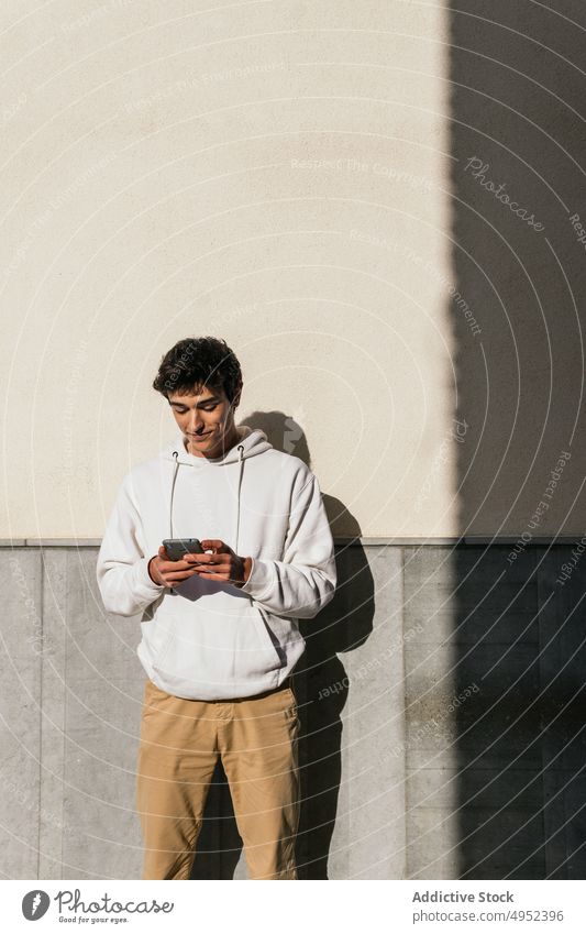 Erfreuter Mann, der auf der Straße eine Nachricht auf seinem Smartphone schreibt Großstadt Browsen Lächeln Surfen männlich benutzend Anschluss Internet urban