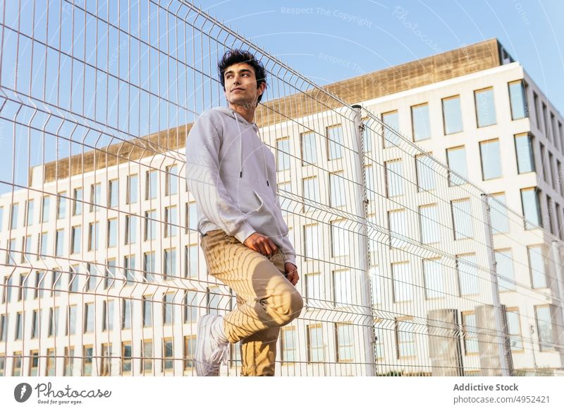 Stilvoller Mann steht in der Nähe von Metallgitter in der Stadt Raster Zaun trendy Outfit Großstadt urban Inhalt männlich jung Straße selbstbewusst