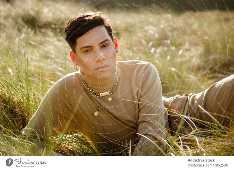 Trendiger ethnischer Mann ruht sich auf einem Feld aus Gras ruhen Landschaft Stil Outfit Sommer Porträt Model männlich sonnig tagsüber lässig Accessoire