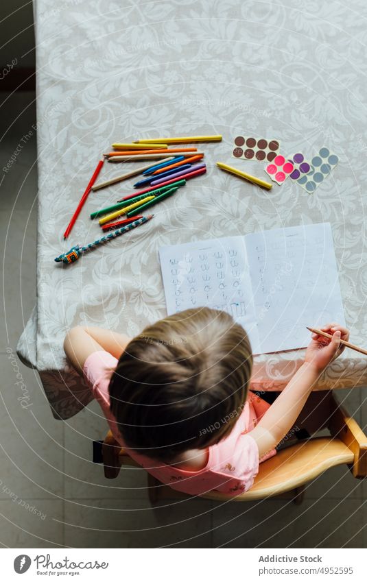 Niedliches kleines Mädchen bei den Hausaufgaben Draufsicht Kind Bildung Papier schreibend gesichtslos sitzen im Innenbereich allein Aufmerksamkeit Schlafzimmer