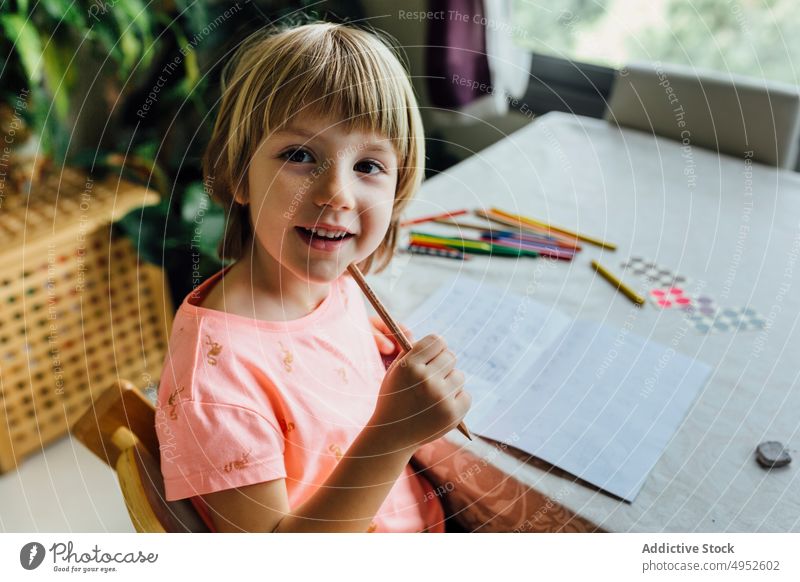 Niedliches kleines Mädchen bei den Hausaufgaben Kind Porträt heiter spielerisch Lächeln Bildung in die Kamera schauen im Innenbereich Glück schreibend sitzen