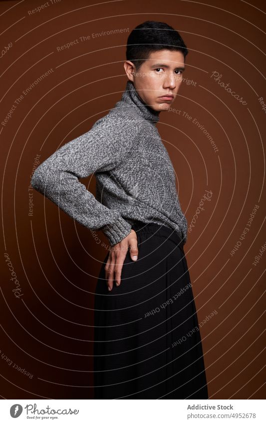 Stilvolles homosexuelles Modell im Pullover auf braunem Hintergrund schwul feminin lgbt Mann emotionslos Porträt gestrickt Stoff Starrer Blick ruhen stehen