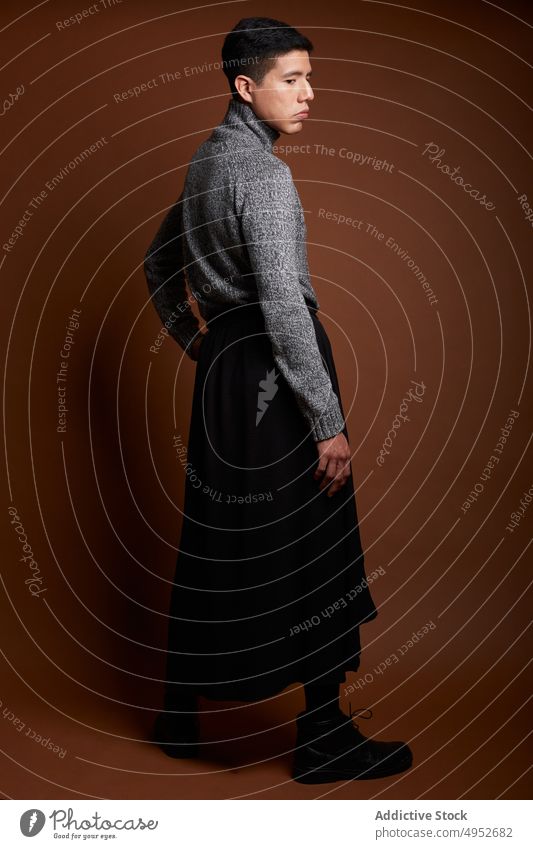 Stilvolles homosexuelles Modell im Pullover auf braunem Hintergrund schwul feminin lgbt Mann emotionslos Porträt gestrickt Stoff Stiefel Leder Starrer Blick