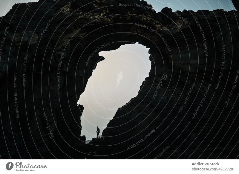 Unbekannter Reisender in der Nähe eines Felsens mit Loch am Tag Golfloch Hochland Fernweh Natur erkunden Geologie Urlaub Mann Ausflug Himmel Oval Form rau hoch