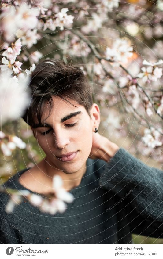 Junger Mann mit geschlossenen Augen unter blühendem Baum Natur im Freien Model Park Blume Mandel Blütezeit Unschärfe Botanik Ast Windstille elegant Umwelt