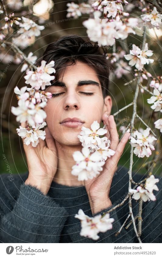 Junger Mann mit geschlossenen Augen unter blühendem Baum Blume Natur Flora Garten Saison Ast im Freien Mandel Blütezeit Unschärfe Botanik Windstille elegant