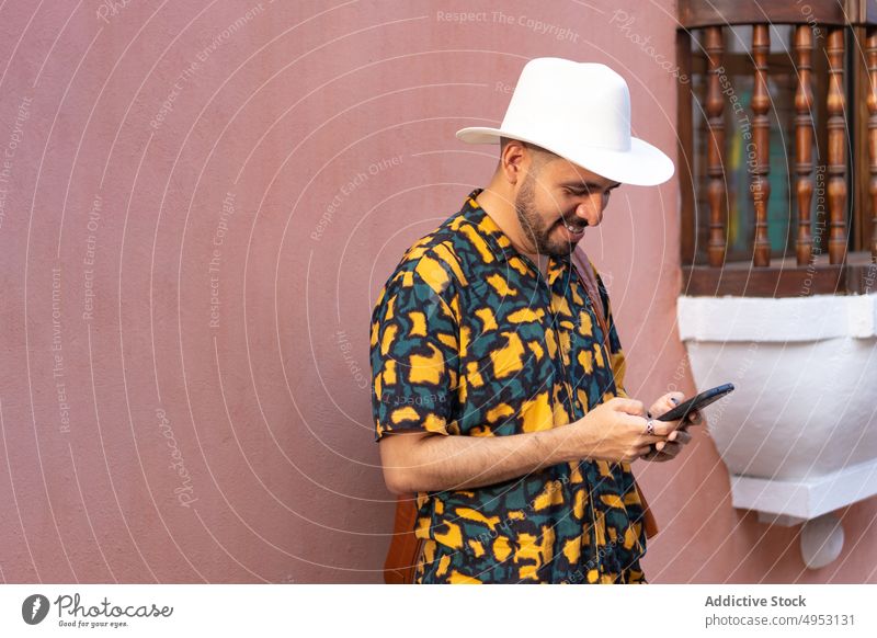 Gut gelaunter Mann, der in der Nähe eines Gebäudes auf seinem Smartphone surft Reisender Tourist Großstadt Straße Ausflug Tourismus Browsen Textnachricht online
