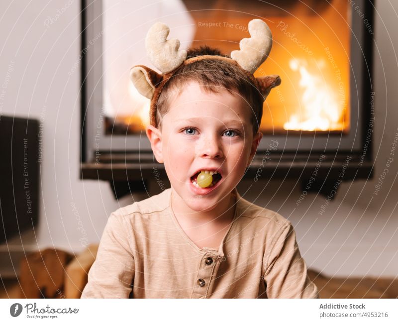 Niedlicher Junge mit Rentiergeweih isst Weintraube Kind Geweih Stirnband Weihnachten Feuerstelle Traube Frucht essen Wohnzimmer Feiertag Anlass heimwärts