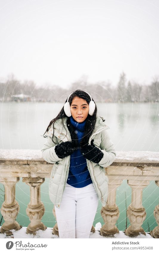 Asiatische Frau unter dem Schnee in der Nähe des Sees im Winter Schneeflocke bewundern Winterzeit Fluss idyllisch Stauanlage urban Porträt Zaun alt Stil