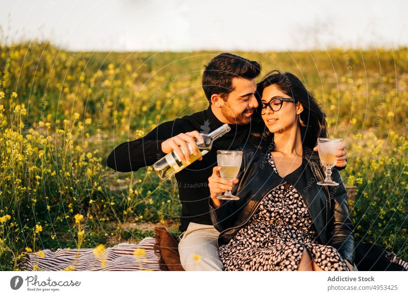 Ethnisches Paar mit einer Flasche Wein auf einer Wiese Partnerschaft Liebe eingießen Zeit verbringen romantisch Wochenende trinken Getränk Alkohol Glas