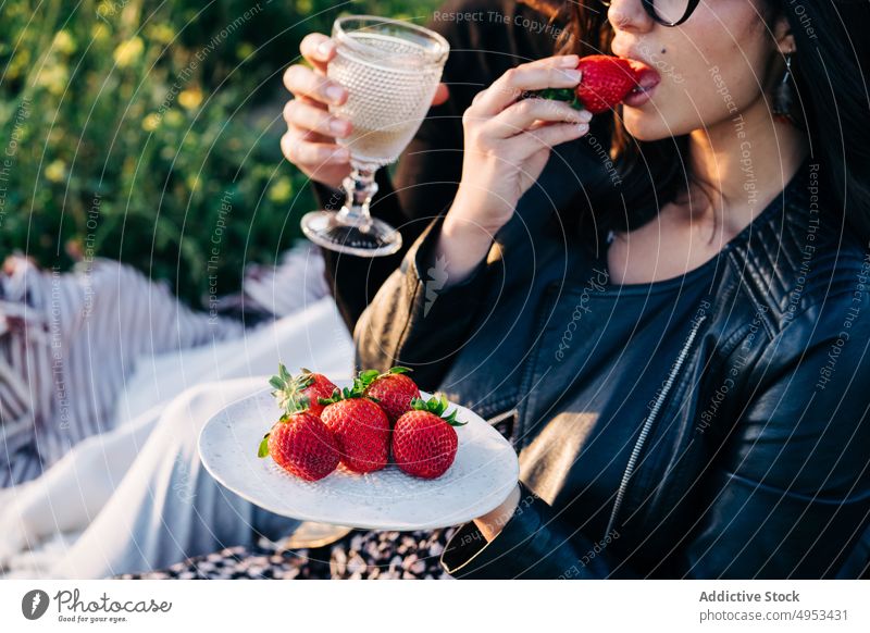 Crop-Frau isst Erdbeere gegen Freund auf Wiese Freundin essen Erdbeeren trinken Alkohol Zeit verbringen Wochenende lecker Rasen Paar Beeren geschmackvoll Teller