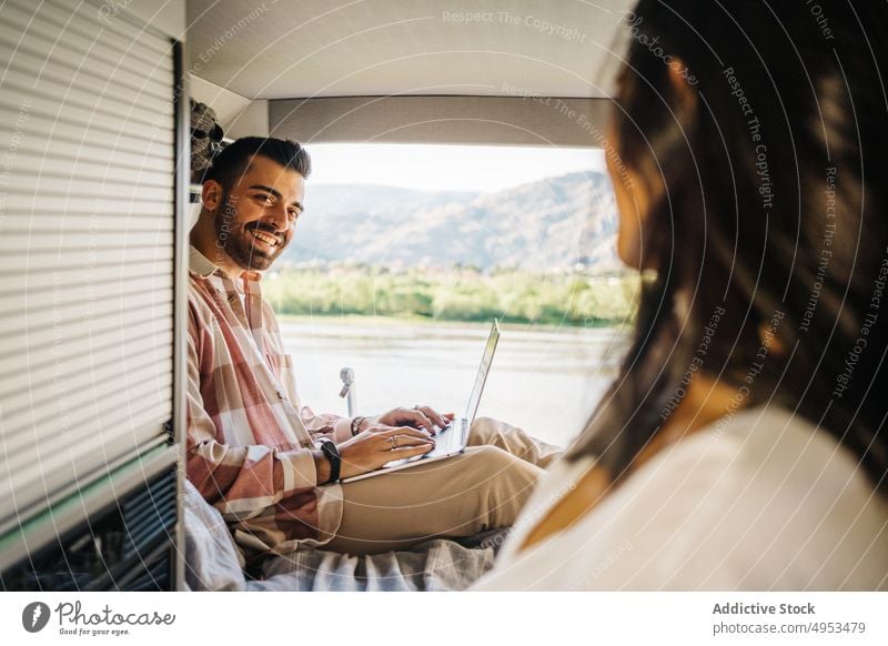 Fröhliches ethnisches Paar von Reisenden im Van reisen Kleintransporter Wohnmobil Zusammensein heiter Arbeit Laptop abgelegen Ausflug hispanisch Apparatur Gerät