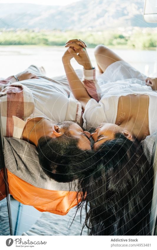 Liebendes hispanisches Paar auf Reisen, das auf einem Bett im Van liegt Reisender Kleintransporter Händchenhalten Angebot Wohnmobil Wohnwagen genießen ethnisch
