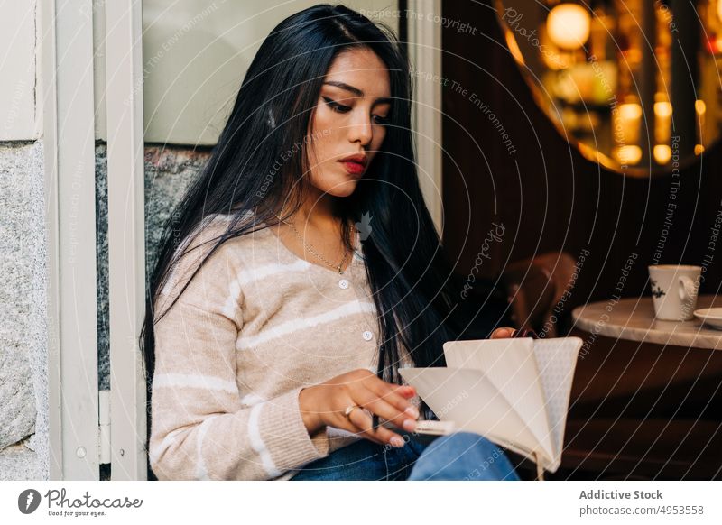 Asiatische Frau schreibt in einem Notizbuch auf der Fensterbank eines Cafés zur Kenntnis nehmen Tagebuch achtsam feminin tausendjährig charmant Schreibstift