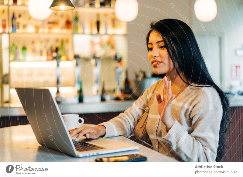 Asiatische Frau mit Video-Chat auf dem Laptop im Cafe Wellenhand Videoanruf Gruß Tippen freie Zeit sprechen Café benutzend Apparatur feminin Gerät Netbook