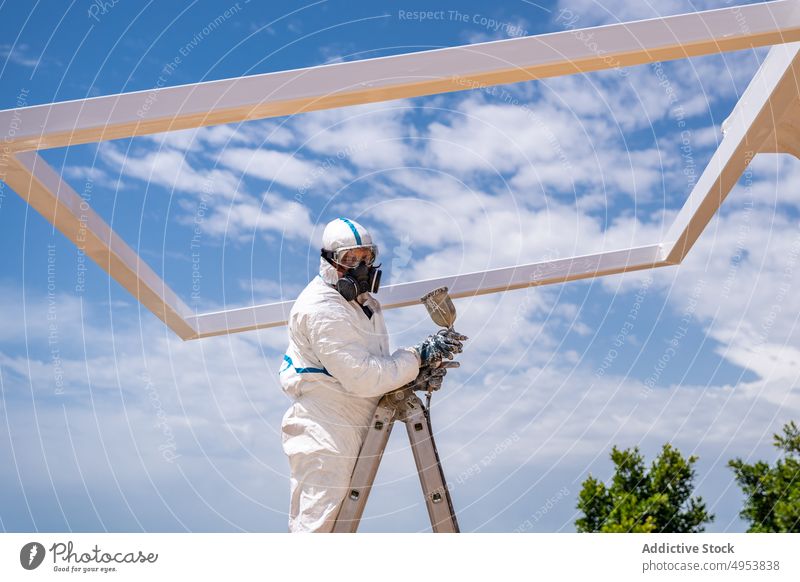 Unbekannter Arbeiter streicht Gebäude an einem sonnigen Tag Farbe Luftbürste Uniform behüten Mundschutz Himmel wolkig tagsüber Laufmasche Job Wehen Mitarbeiter