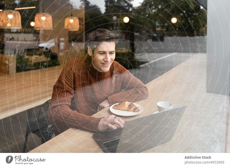 Gut gelaunter Mann mit Laptop, der in einem Café mit seinem Smartphone spricht reden Kaffee Glück Videoanruf Fenster jung Schüler freiberuflich Pause Frühstück