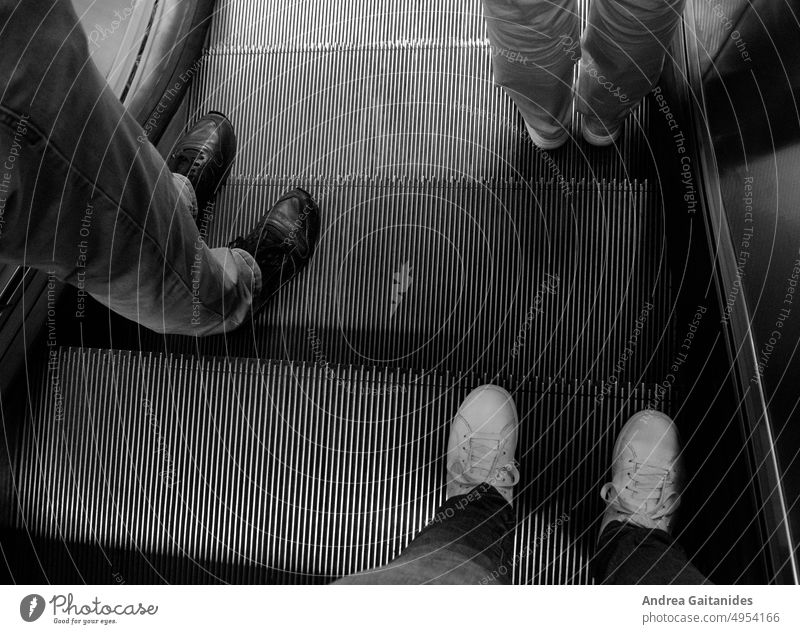 Füße dreier Personen auf einer Rolltreppe, Blick von oben, horizontal Beine Schuhe Turnschuhe Sneakers urban städtisch Stadt Bahnhof Treppe modern warten
