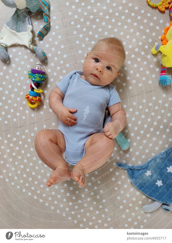 Neugieriger, hübscher Babyjunge in blauem Körper, der auf einer Spielmatte liegt und in die Kamera schaut Junge bezaubernd neugeboren Kind Kindheit Süßer