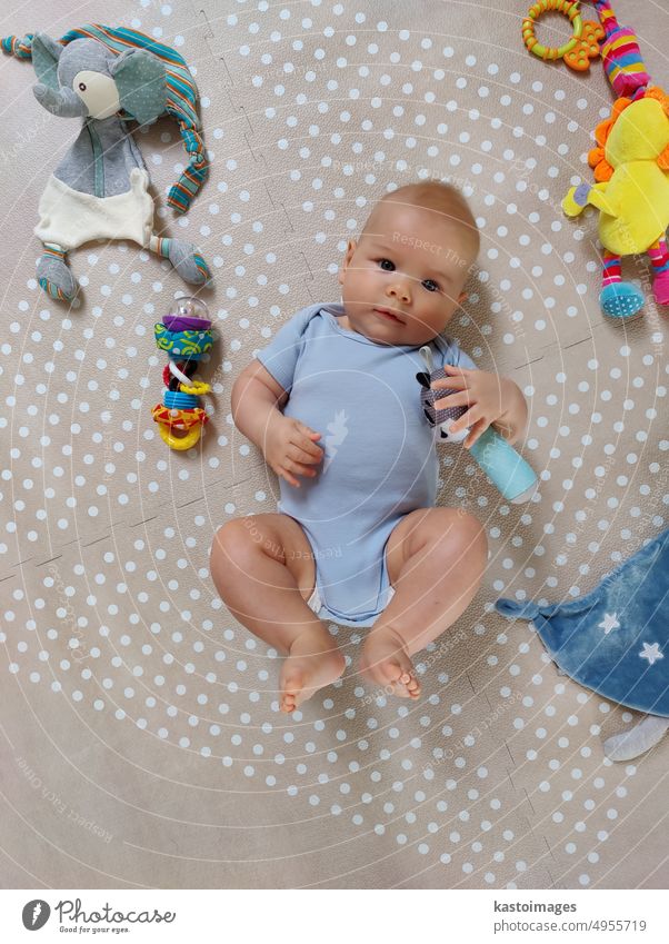Neugieriger, hübscher Babyjunge in blauem Körper, der auf einer Spielmatte liegt und in die Kamera schaut Junge bezaubernd neugeboren Kind Kindheit Süßer