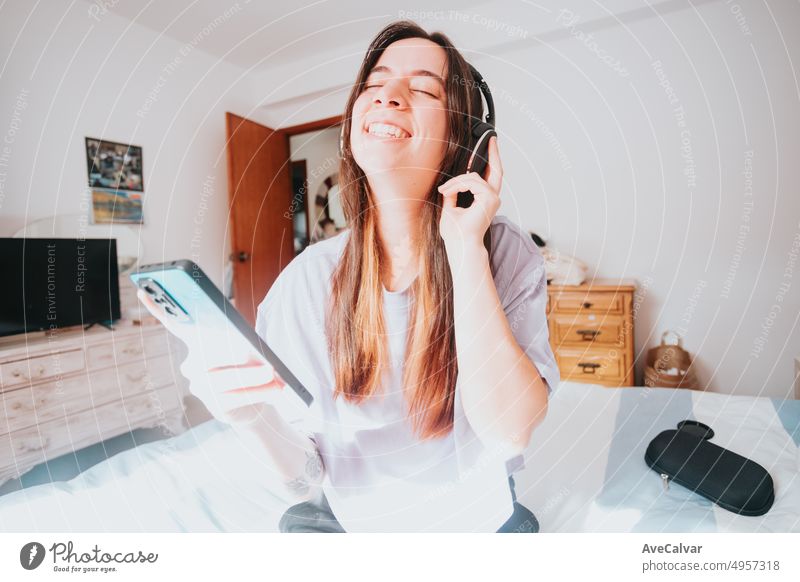 Glückliche und enthusiastische Frau, die das Leben genießt und Musik oder ihren Lieblingspodcast mit ihrem Mobiltelefon und drahtlosen Kopfhörern im Schlafzimmer hört. Freizeitaktivitäten, junge Menschen neue Art des Streamings