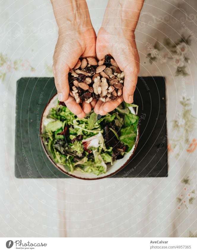 Nahaufnahme von Händen, die mehrere Nüsse, Walnüsse, Rosinen und Mandeln über einer Salatschüssel mit Salat halten, um eine vegane Mahlzeit mit Nährstoffen, Kalorien und Proteinen zu vervollständigen, die ausreichend Energie liefern