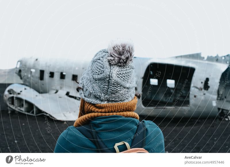Frau in Winterkleidung vor dem Wrack des abgestürzten Flugzeugs in Island, am Strand von Sólheimasandur. Reisen nach Island, Road Trip Konzept. Kopieren Sie Raum Bild, besuchen Island.