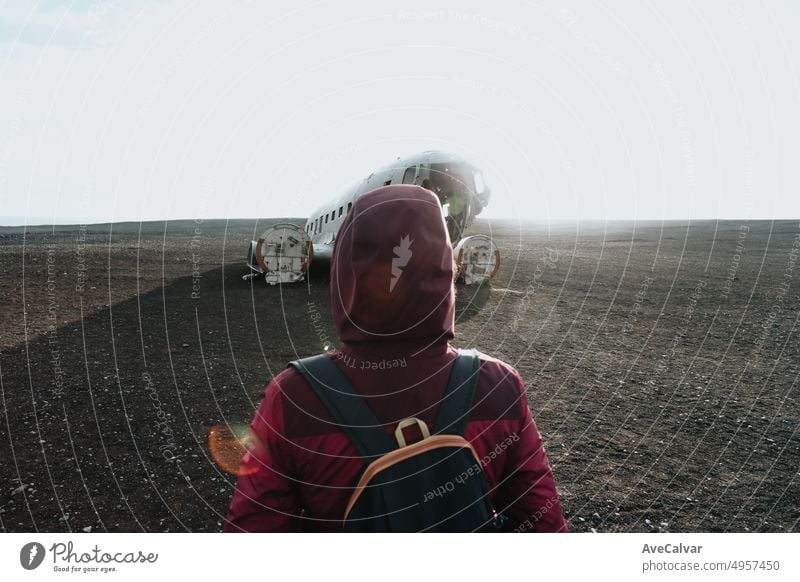 Frau in Winterkleidung vor dem Wrack des abgestürzten Flugzeugs in Island, am Strand von Sólheimasandur. Reisen nach Island, Road Trip Konzept. Kopieren Sie Raum Bild, besuchen Island.