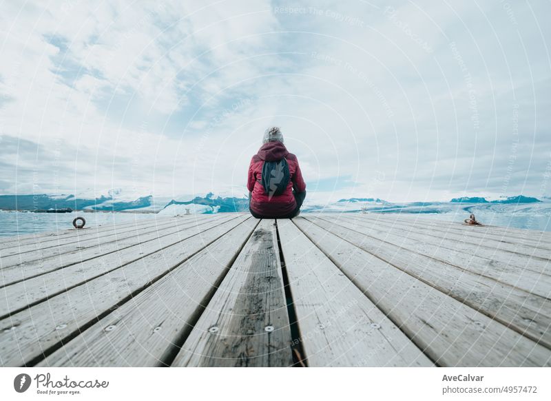 Junge Frau Reisende zurück Schuss sitzen auf den Docks entspannen und denken vor den Gletschern von Jökulsárlón in Island. Platz zum Kopieren. Lebe deinen Traum, Liebe in Island, Roadtrip-Stil