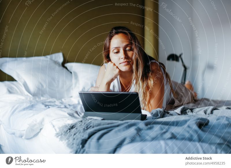Junge Frau sieht sich im Schlafzimmer einen Film auf einem Tablet an Bett Tablette benutzend Komfort Gerät Anschluss Kälte jung Decke weich Lügen Apparatur