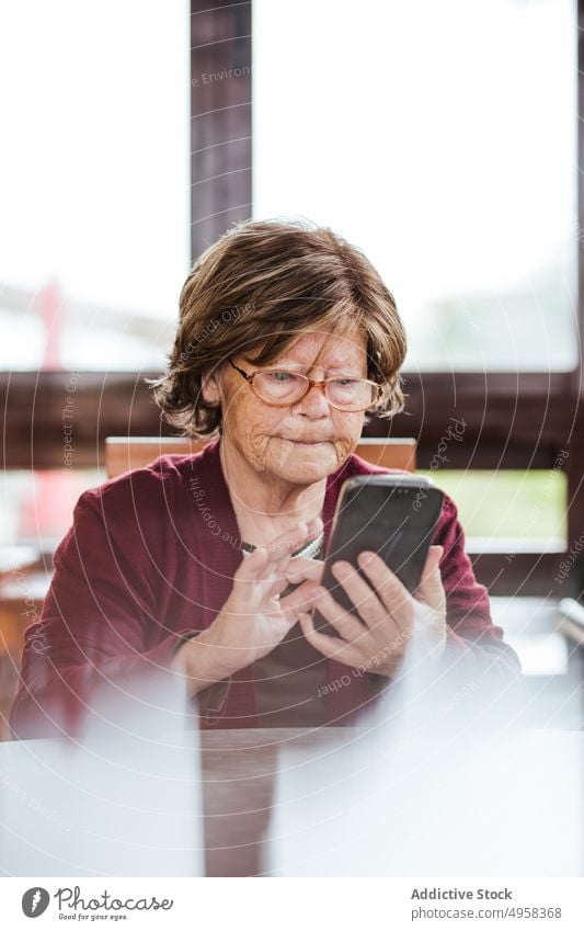 Ältere Frau mit Smartphone am Tisch benutzend heimwärts älter soziale Netzwerke sitzen ruhen Rentnerin Senior Brille Browsen Gerät Apparatur Internet online
