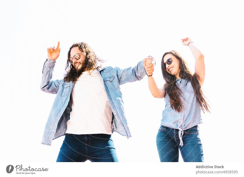 Glückliches ethnisches Paar mit Sonnenbrille tanzt auf weißem Hintergrund Händchenhalten Tanzen Spaß haben Partnerschaft heiter Lifestyle nach oben zeigen