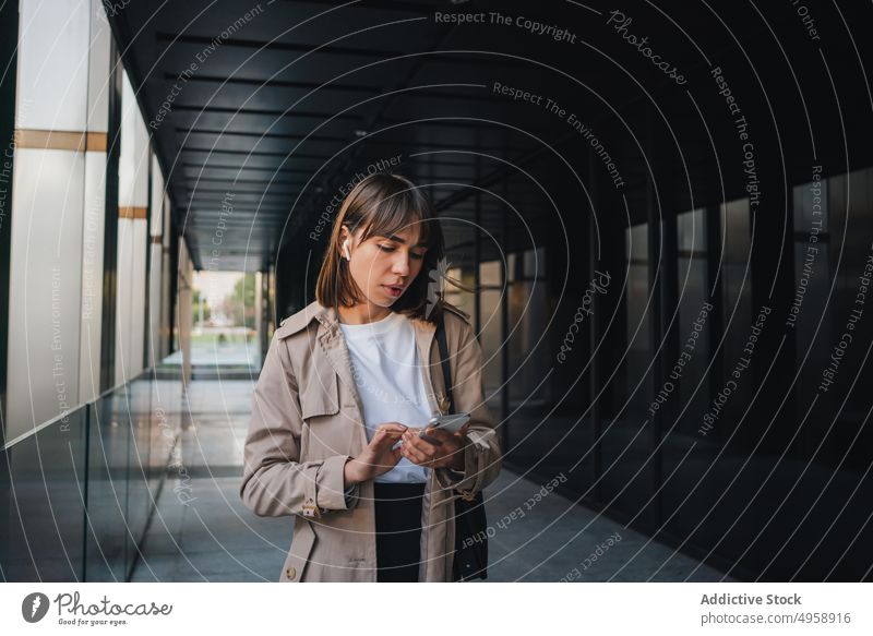 Junge Frau mit Kopfhörern, die in der Nähe eines Gebäudes telefoniert modern Smartphone Video-Chat Kommunizieren Zaun Browsen zuschauend Gespräch urban trendy