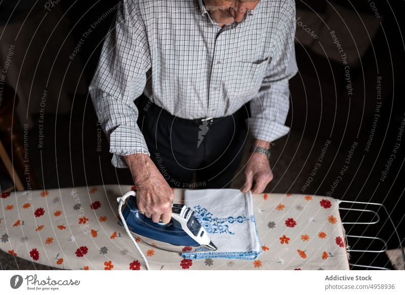 Anonymer älterer Mann bügelt Textilien im Zimmer gealtert Senior bügeln Arbeit Hausarbeit Routine reif Fokus heimwärts männlich lässig Gewebe heimisch zu Hause