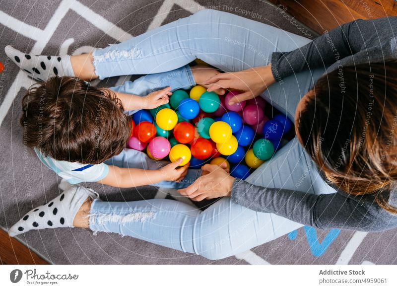 Anonyme Mutter und Sohn spielen mit Bällen auf dem Boden Ball Stock sitzen Haufen Spielzeug farbenfroh Kinderzimmer heimwärts Himmel und Hölle Unterlage wenig