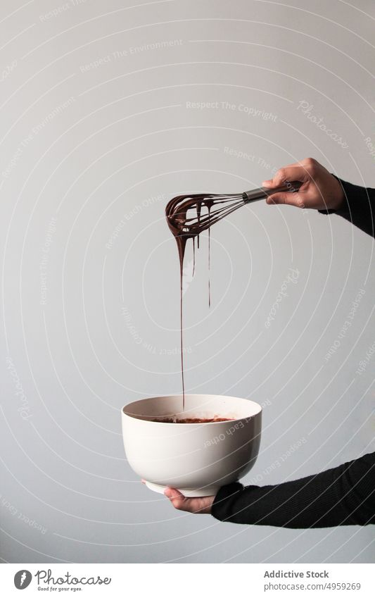 Crop-Hände, die Schokolade von einem Schneebesen abtropfen lassen süß lecker Lebensmittel Dessert Sahne Tropfen Essen zubereiten liquide mischen braun Bonbon