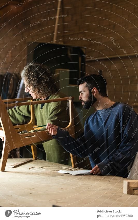 Handwerker, der einen Holzstuhl herstellt, während ein Kollege Skizzen zeichnet Männer Tischlerin Mitarbeiterin messen Klebeband Stuhl Werkstatt Tischlerarbeit