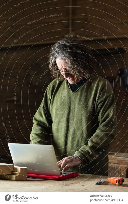 Lächelnder männlicher Holzarbeiter, der einen Laptop für seine Arbeit benutzt Mann Tischler Tippen benutzend Hobelbank Schreinerei positiv beschäftigt