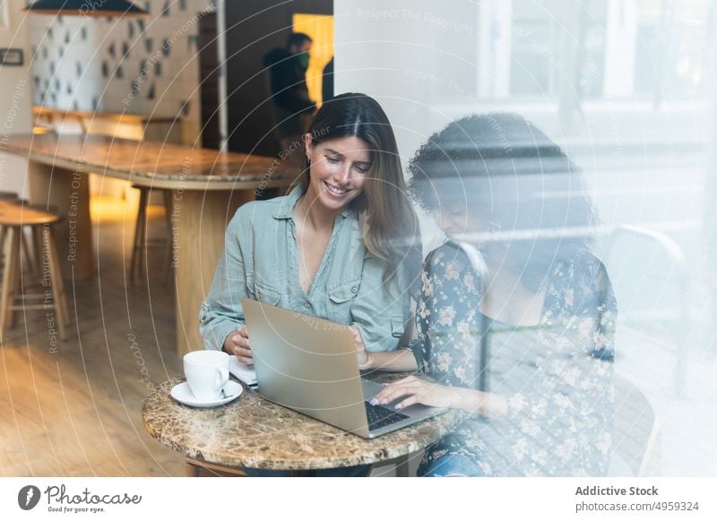Lächelnde multirassische Freundinnen teilen sich einen Laptop in einem Café bester Freund Internet online Zeitvertreib Frauen benutzend Apparatur Wochenende