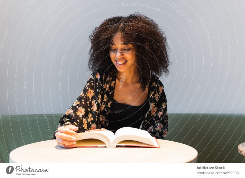 Ethnische Frau liest ein Buch am Cafétisch lesen Glück Literatur Lächeln Wissen Bildung Freizeit feminin Freude Tasse Kaffee Inhalt Heißgetränk Getränk