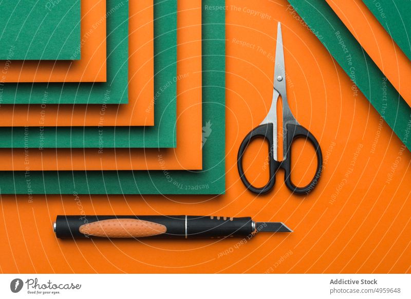 Schere und Cutter auf grünem und orangefarbenem Kartonhintergrund Sauberkeit Ausschnitt Farbe farbenfroh Konzept Handwerk geschnitten Kutter Design geometrisch