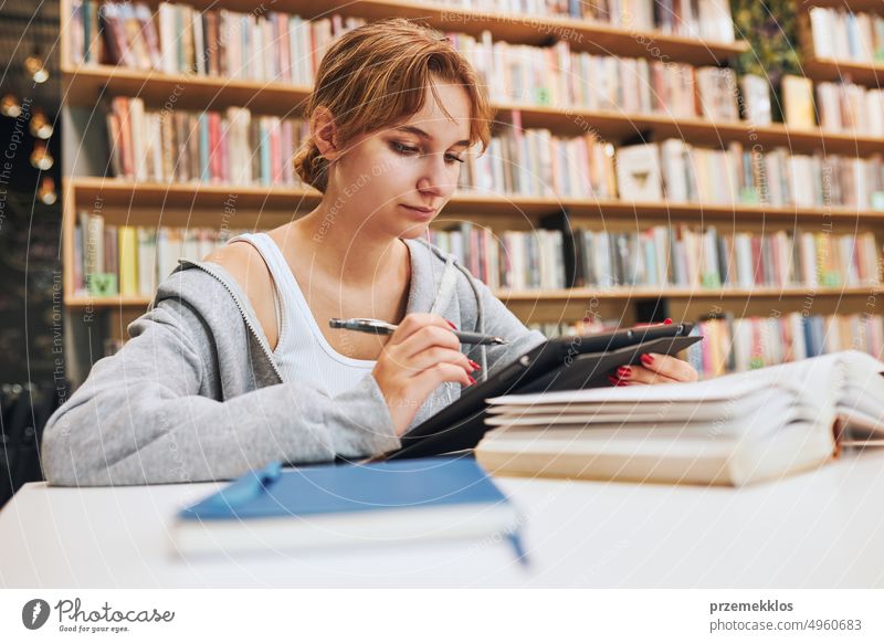 Studentin lernt in der Universitätsbibliothek. Junge Frau schreibt Aufsatz und macht Notizen mit Computer-Tablet. Konzentrierter Student, der für College-Prüfungen lernt