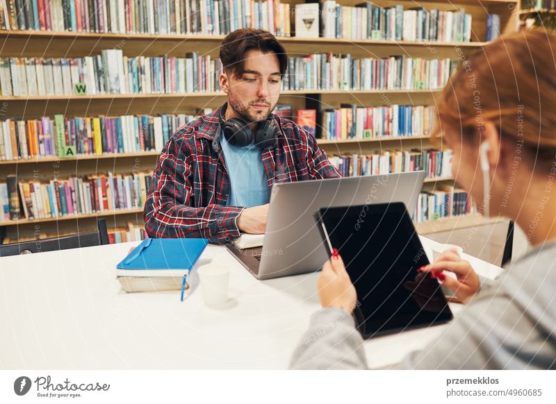 Studenten lernen in der Universitätsbibliothek. Mädchen schreibt Aufsatz und macht Notizen mit Hilfe von Technologie. Junger Mann beim Videokurs am Laptop. Studenten lernen für College-Prüfungen