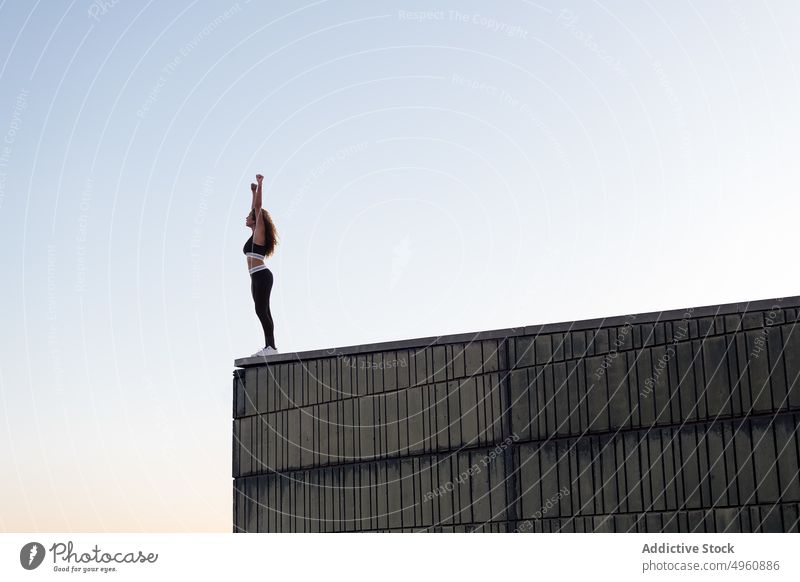 Anonyme Sportlerin mit erhobenen Armen auf dem Dach unter hellem Himmel Sportbekleidung Arme hochgezogen Freiheit bewundern Vitalität Energie Sonnenuntergang