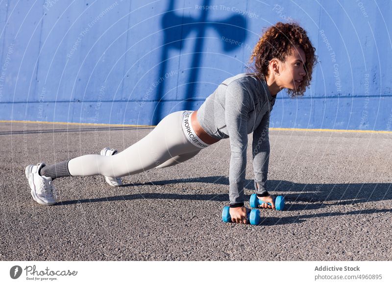 Entschlossene Sportlerin beim Training mit Hanteln auf einer städtischen Straße Schiffsplanken Kurzhantel Ausdauer Motivation Stärke Frau stark Kraft
