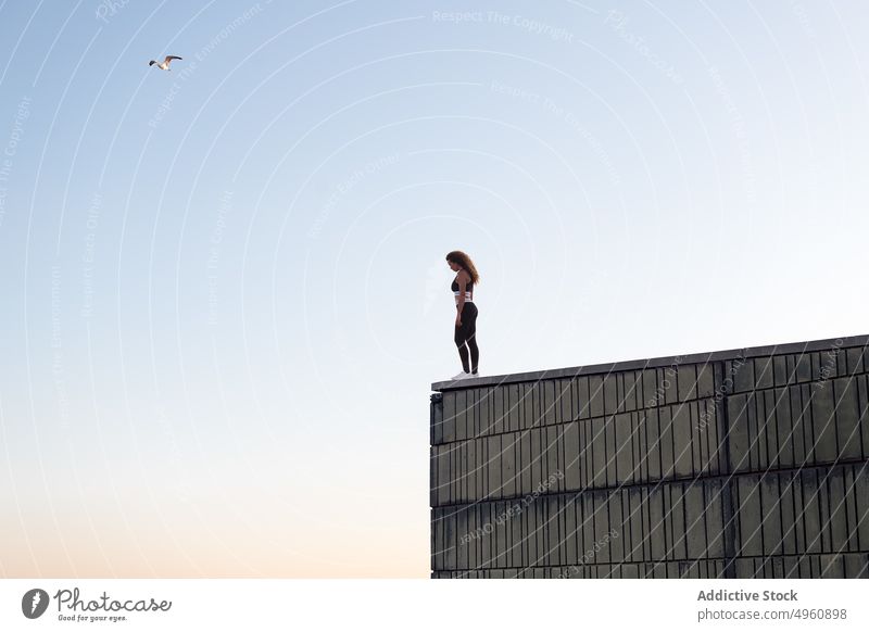 Anonyme Sportlerin auf dem Dach unter hellem Himmel ruhend Sportbekleidung Freiheit aussruhen bewundern Vitalität Energie Sonnenuntergang Frau stehen genießen