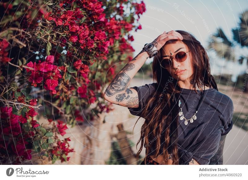 Frau mit Sonnenbrille vor Busch mit bunten Blumen im Park cool Tattoo auflehnen Verlockung Piercing Bindi Vorschein brünett Auge Starrer Blick trendy Tradition