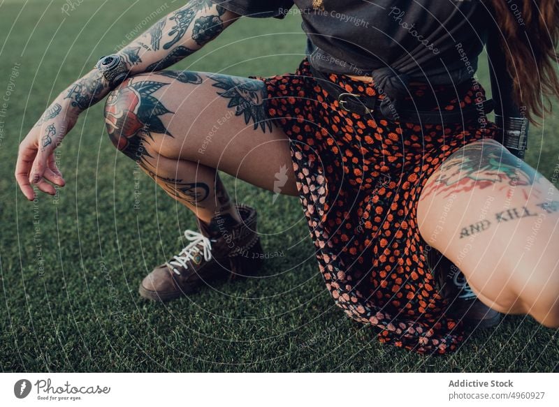 Stilvolle tätowierte Millennial-Frau auf Rasen Tattoo brünett Bein cool auflehnen trendy provokant hockte Mode traumhaft Individualität Turnschuh stilvoll